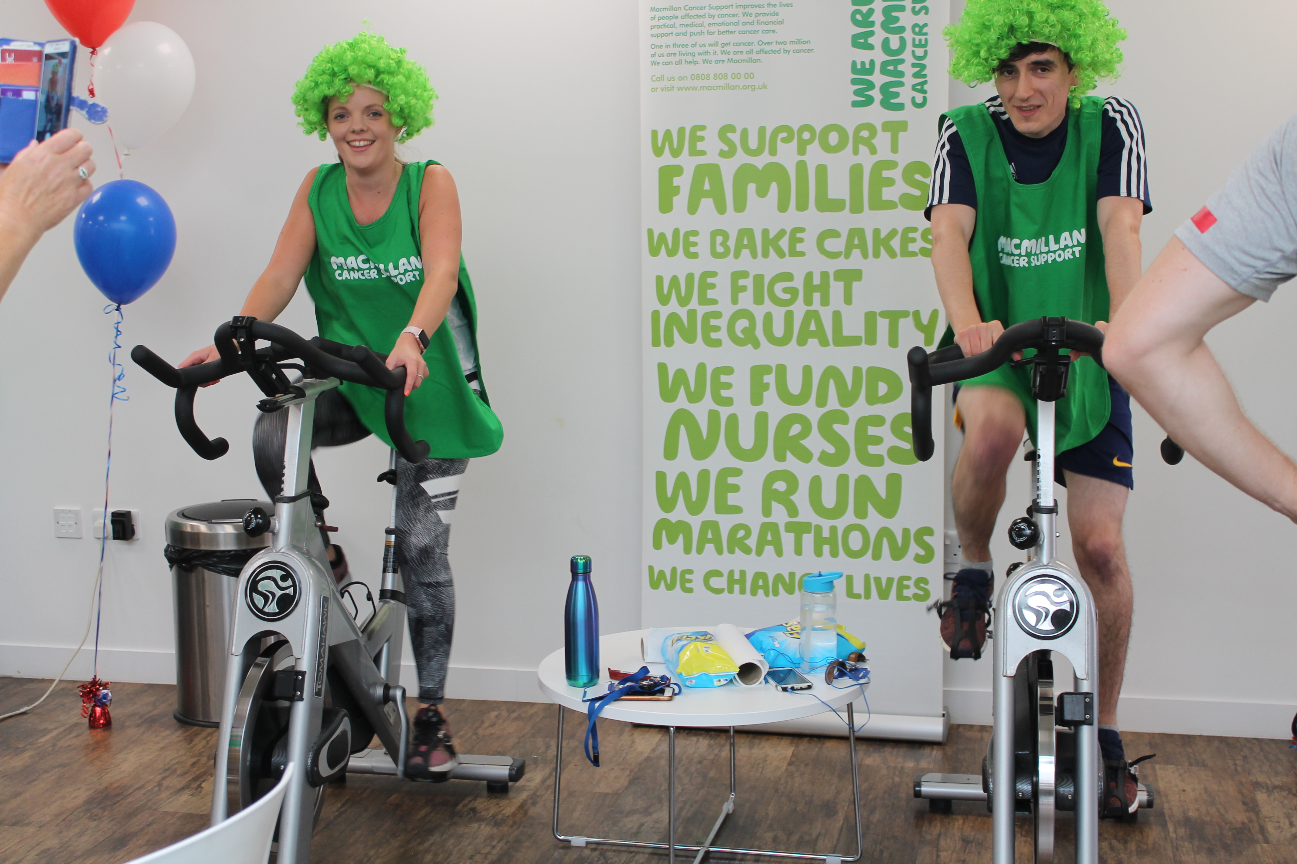 CliniMed staff riding on the training bikes whilst wearing green wigs